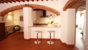 A kitchen with a brick archway, two bar stools, a countertop, and a hanging light fixture. - "Il Focolare" Superior Apartment in Monticchiello (Monticchiello)