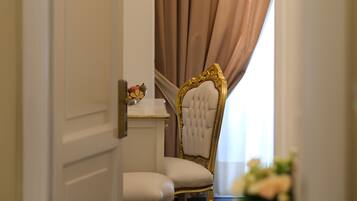 A room with a white door, a chair with gold detailing, a white table, and a curtain.