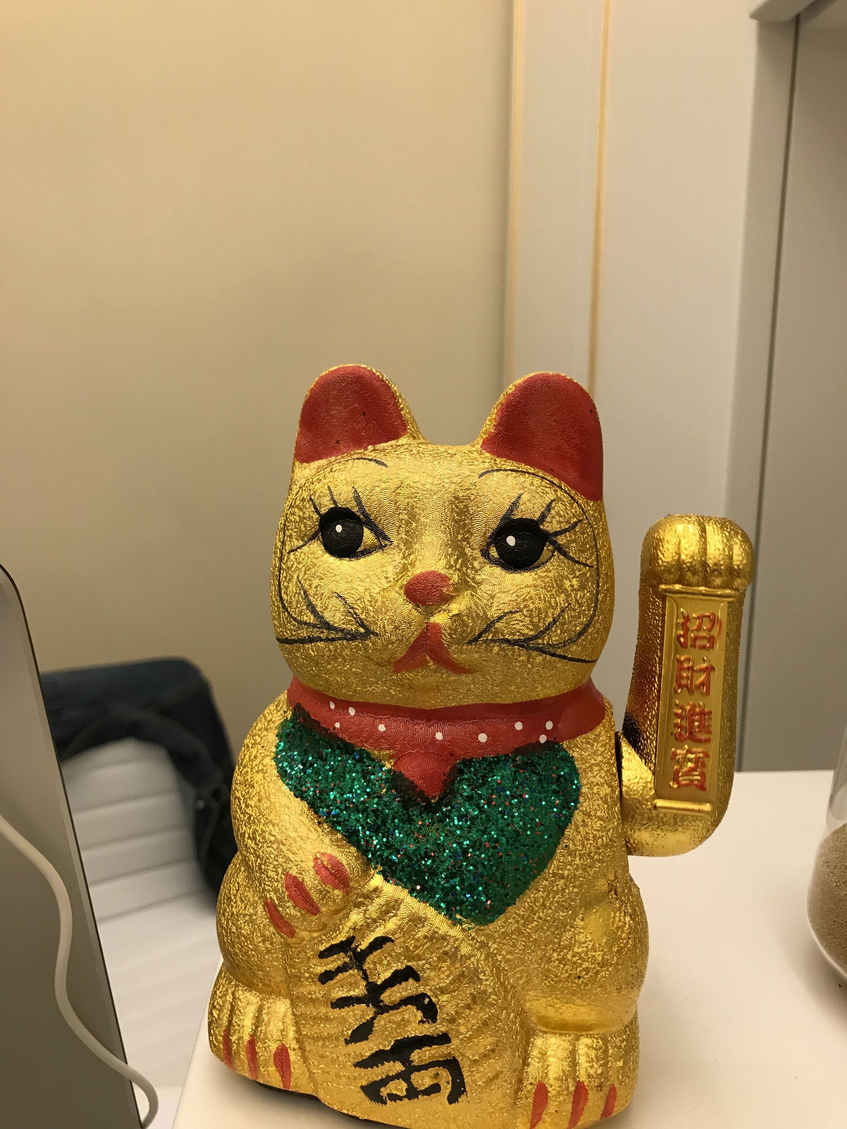 A golden cat figurine with a red collar and a scroll, placed on a white surface.