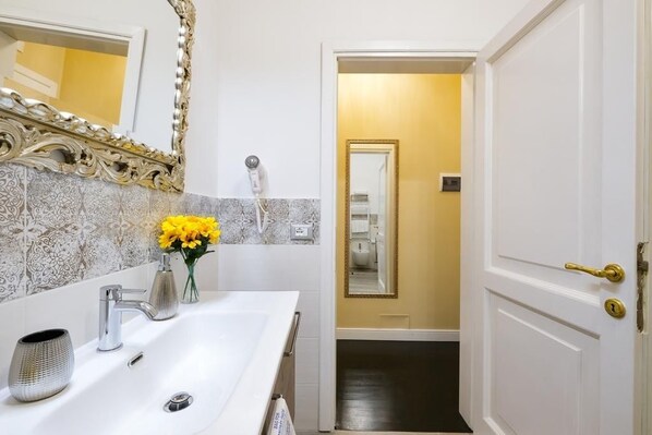 A bathroom with a white sink, a mirror with an ornate frame, and a door leading to a hallway.
