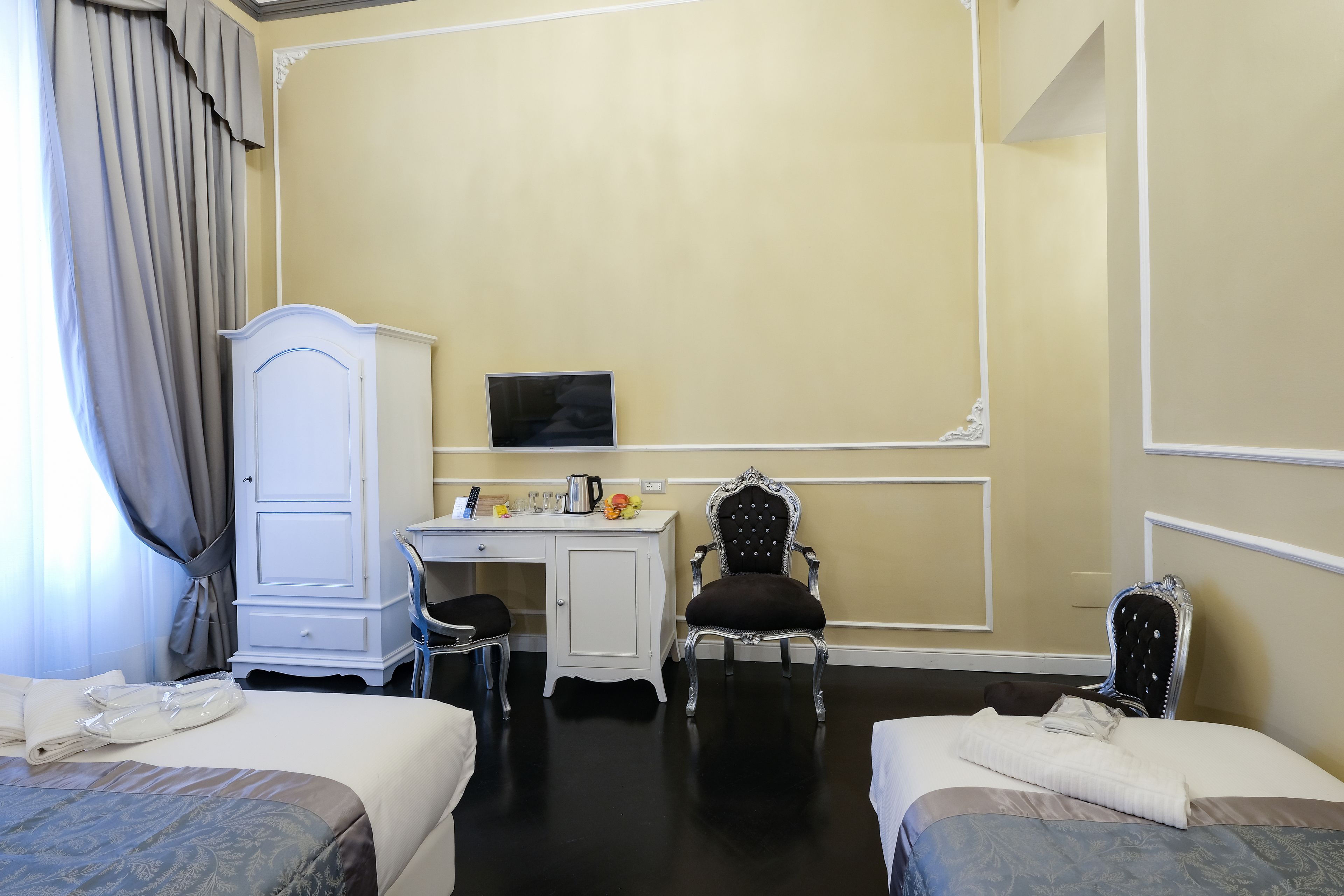 A hotel room with two beds, a desk, a chair, and a television.