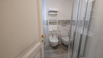 Une salle de bain équipée d’un bidet, de toilettes et d’une douche à parois en verre.