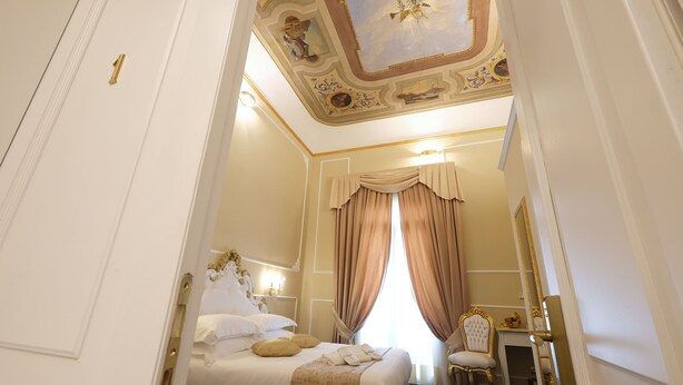 A luxurious bedroom with a large bed, a vanity with a mirror, and a ceiling with ornate decorations. - B&B Kingsman (Florence)