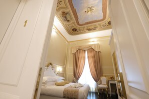 A luxurious bedroom with a large bed, a vanity with a mirror, and a ceiling with ornate decorations.