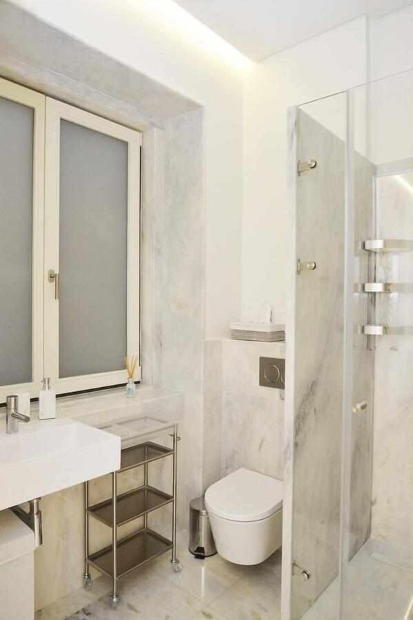 A modern bathroom with a white sink, a glass shower enclosure, and a toilet. - Trendy Chic - Checkinhome (Lisboa)