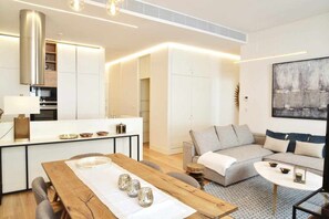 A modern living room with a grey sofa, a wooden dining table, and a kitchen area with white cabinets and a central island. - Trendy Chic - Checkinhome (Lisboa)