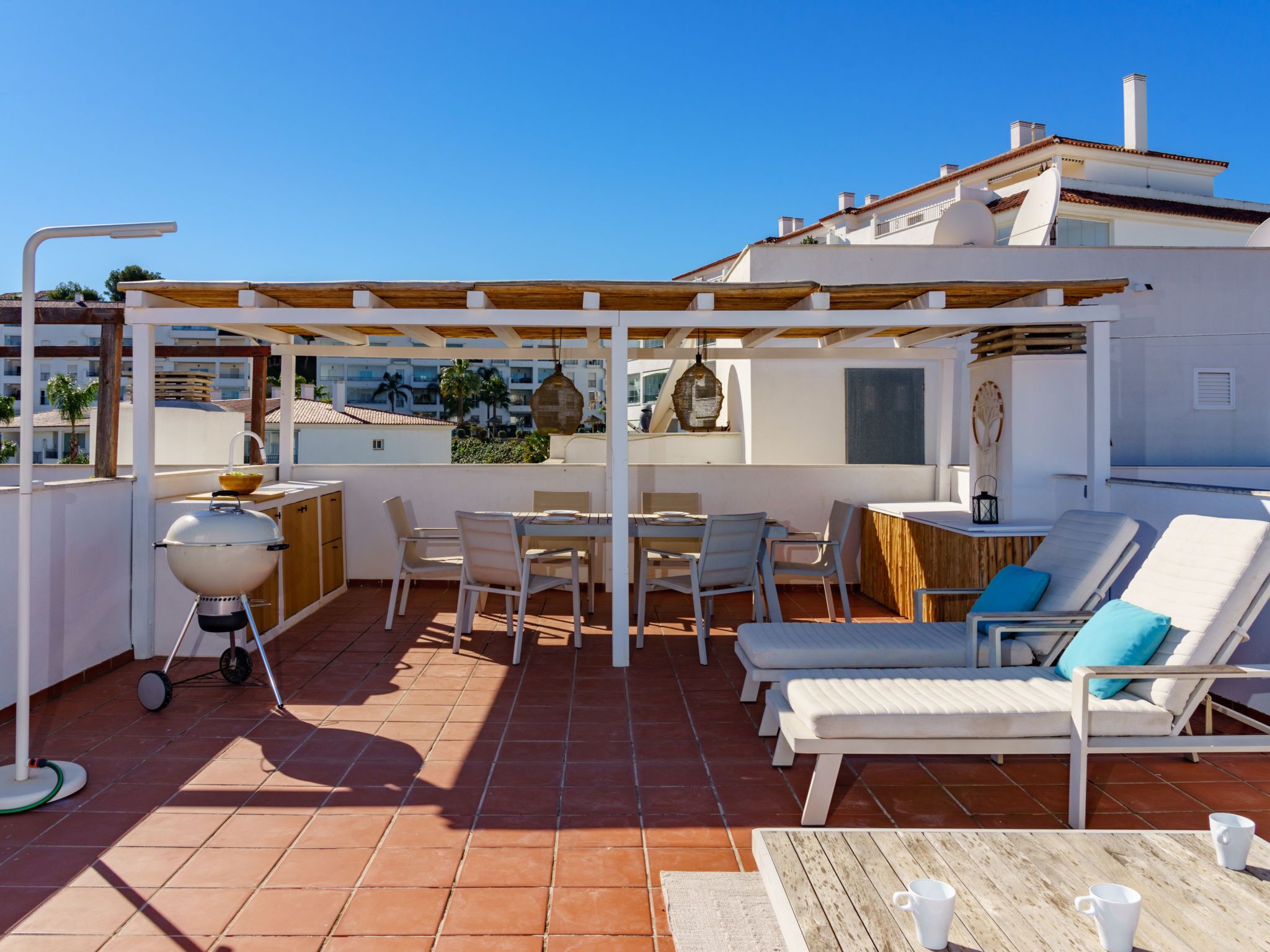 A rooftop terrace with a barbecue, dining area, lounge chairs, and a view of the city.