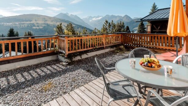 A terrace with a wooden railing, a round glass table, and chairs. There is a bowl of fruit on the table. - Lena Top 2 by Interhome (Königsleiten)