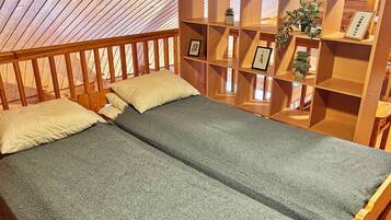 A single bed with a grey mattress and two pillows, a wooden headboard, and a wooden shelving unit with a plant and framed pictures.
