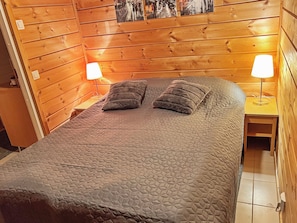 A wooden-paneled room with a bed, two bedside lamps, and a wall-mounted picture. - Saunaharju 4 by Interhome (Lieksa)