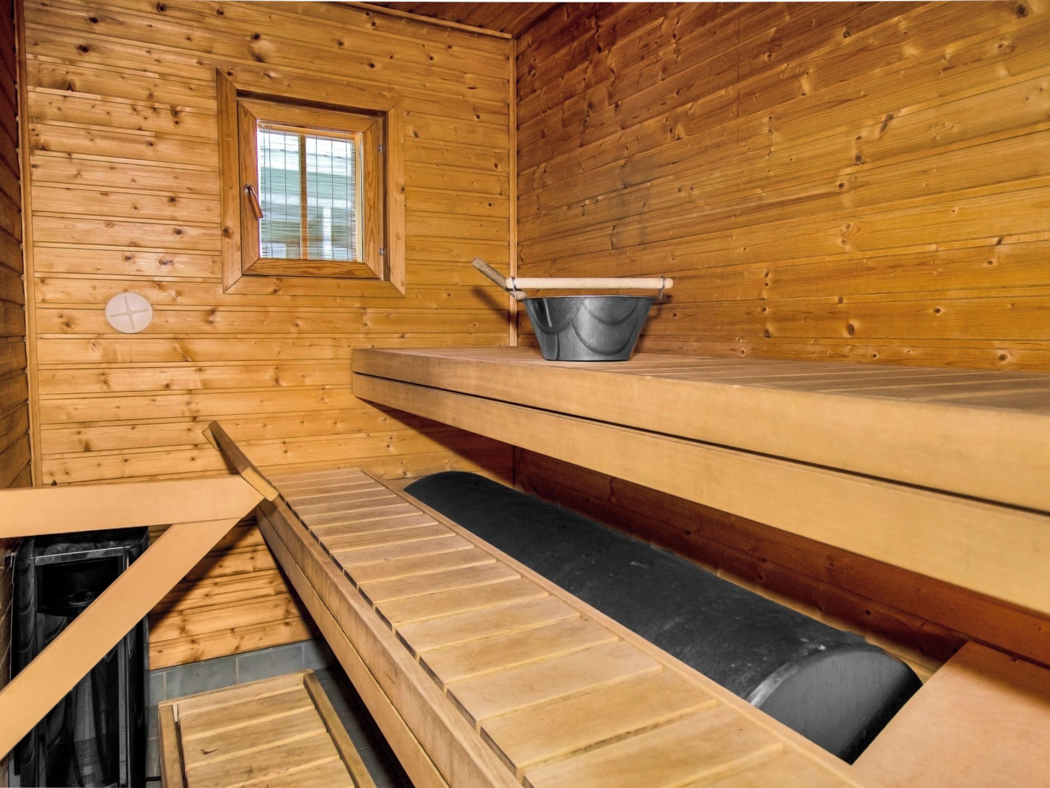 Un sauna avec des murs en bois, une fenêtre, un banc et un récipient en métal.