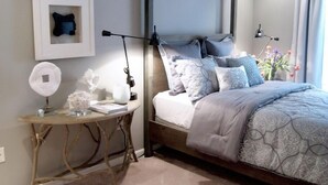 A bedroom with a four-poster bed, a bedside table with a lamp, a framed picture, and a vase with flowers. - Community has three pools & tennis courts (Rehoboth Beach)