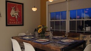 A dining area with a table set for four, a framed poster on the wall, and a window with blinds. - Community has three pools & tennis courts (Rehoboth Beach)
