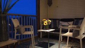 A covered patio area with two white chairs, a small table with a vase of flowers, and a bench with striped cushions. - Community has three pools & tennis courts (Rehoboth Beach)
