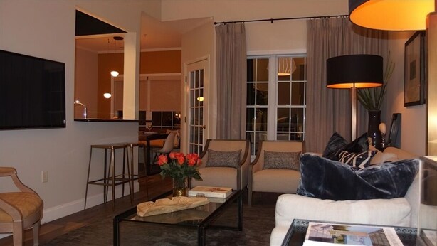 A living room with a sofa, armchairs, a coffee table, and a TV. There is a door leading to another room and a window with curtains. - Community has three pools & tennis courts (Rehoboth Beach)