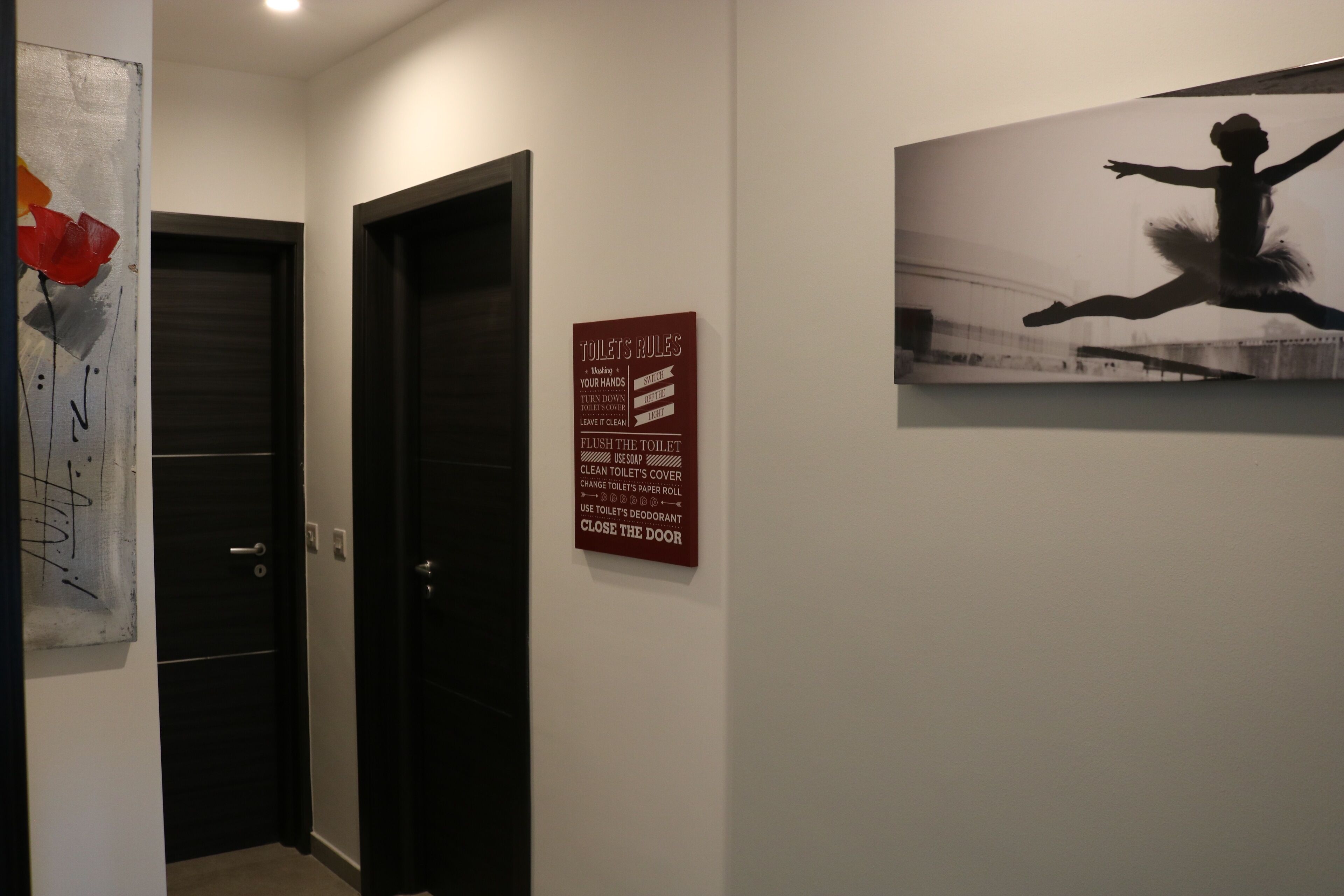 A hallway with two doors, a wall-mounted sign with toilet rules, and a black and white photograph.