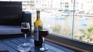 A table with two wine glasses and a bottle of wine, overlooking a marina with boats. - Seaside Apartment (Marsaskala)