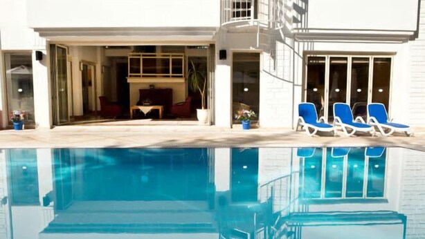 A swimming pool with lounge chairs, a patio area, and a building with large windows. - Villa Gizem (Manavgat)