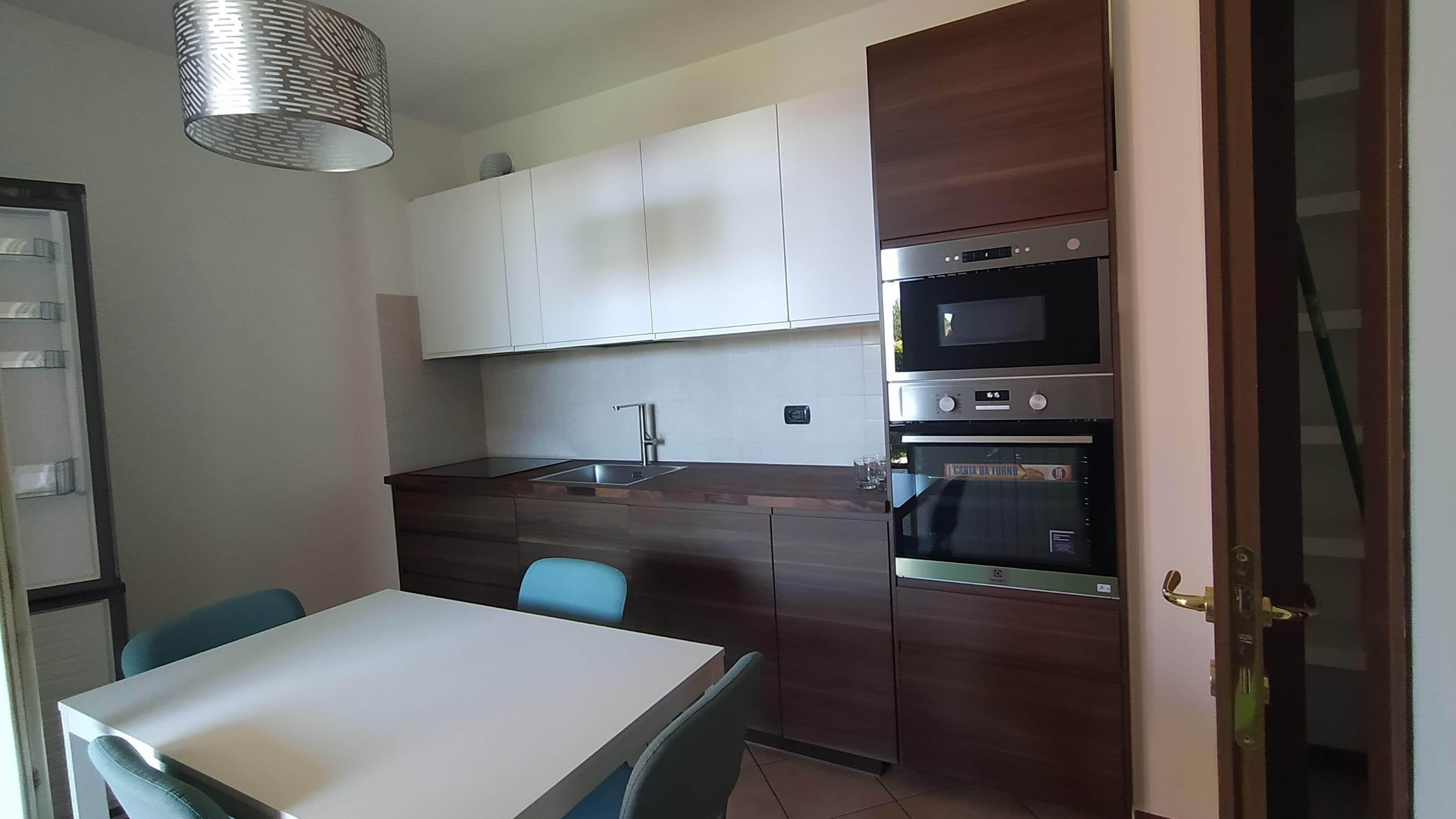 A compact kitchen with white cabinets, a built-in oven, and a dining table with chairs.