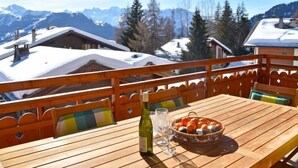 Una terraza de madera con una mesa dispuesta para dos personas, una botella de vino y una cesta de fruta.