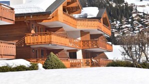 Una cabaña de madera de varios pisos con balcones, frente a un paisaje nevado de montañas.