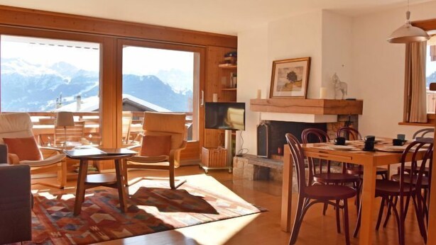 Amplia sala de estar con un ventanal que da a montañas, una chimenea y un comedor con muebles de madera.