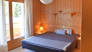 A wooden-paneled bedroom with a bed, a bedside lamp, and a hanging light fixture. - Romarin 220 by Interhome (Verbier)
