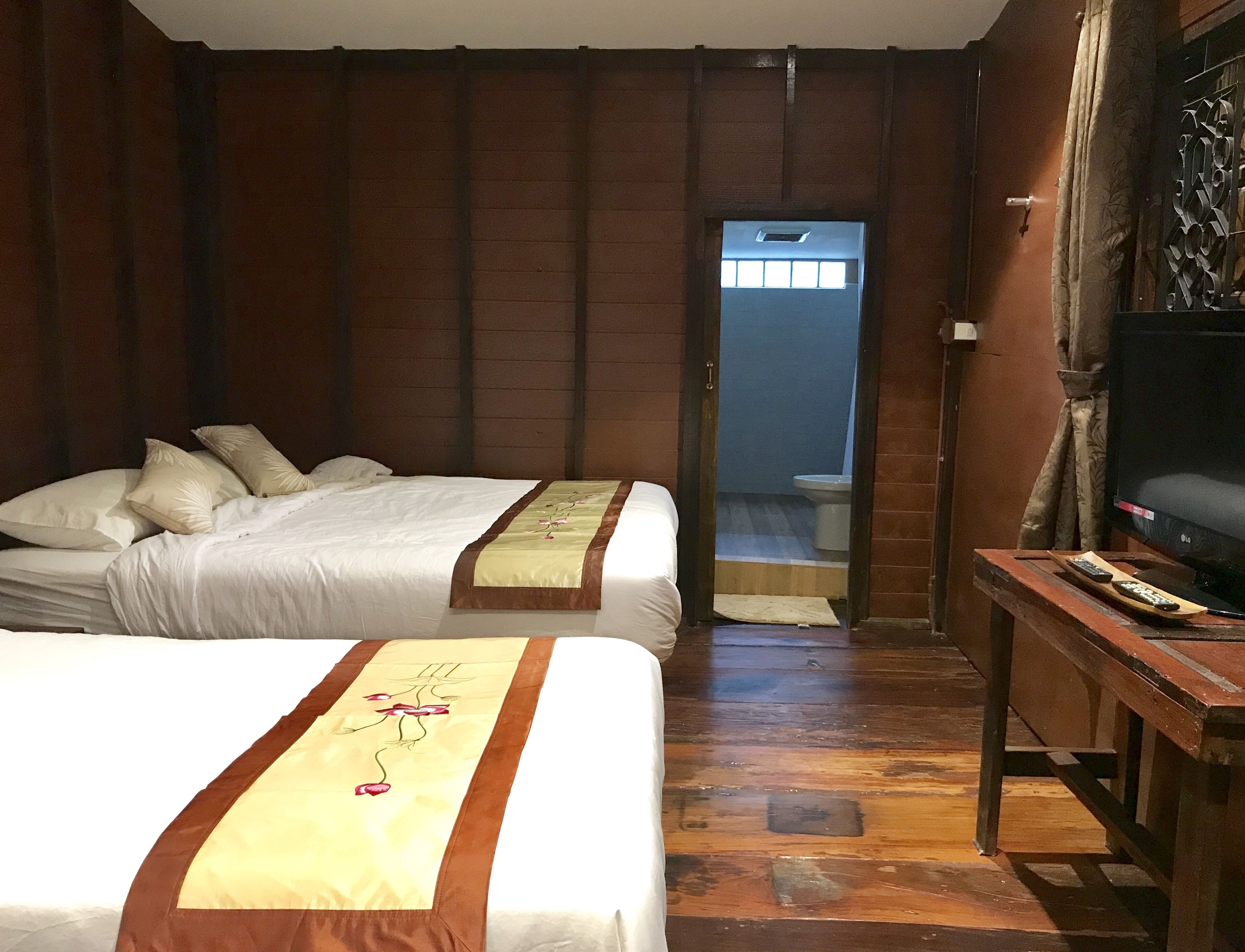 A hotel room with two beds, a wooden floor, a television, and a bathroom visible through an open door.