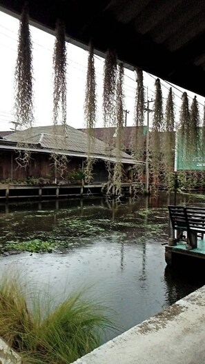 A covered outdoor area with a water body, a wooden structure, and a bench. - Reuan Vilawan (Damnoen Saduak)