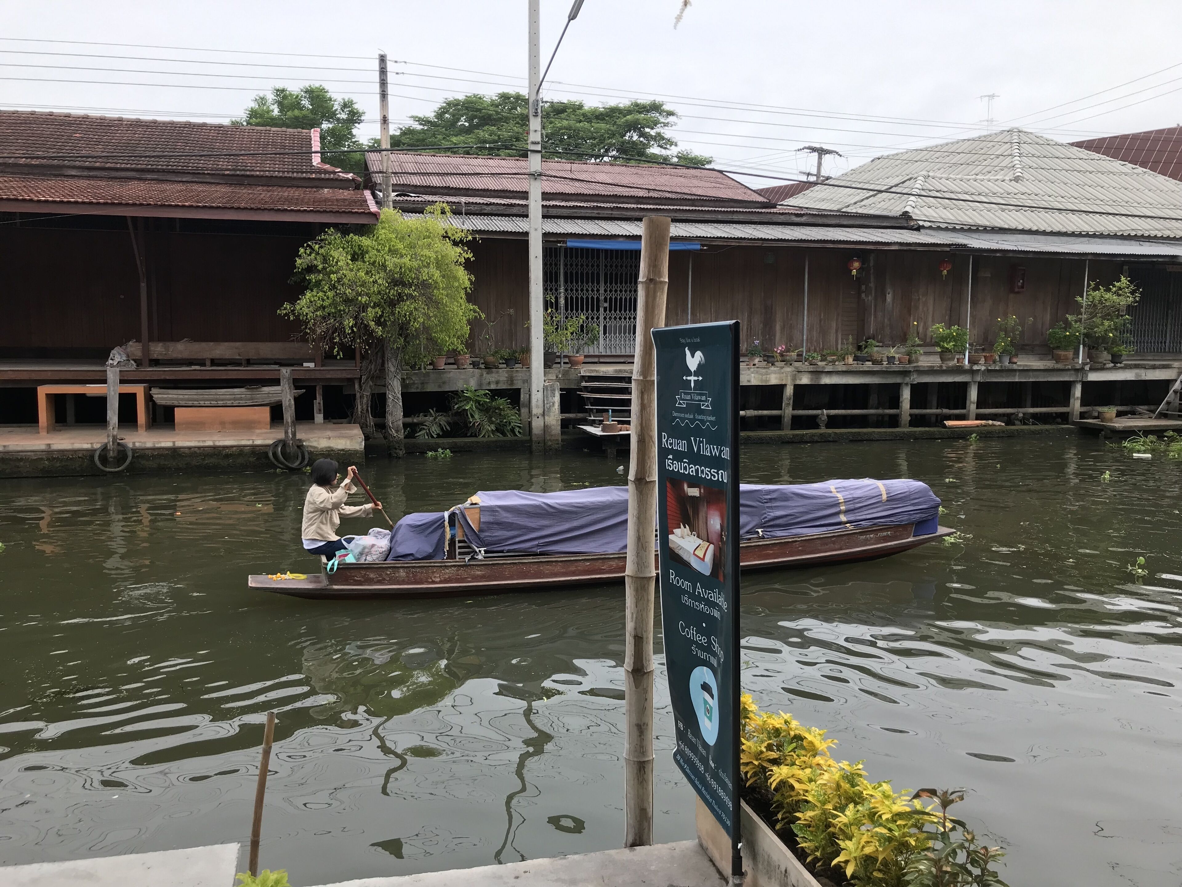 A boat with a person rowing, a signboard, and a building with a tiled roof.