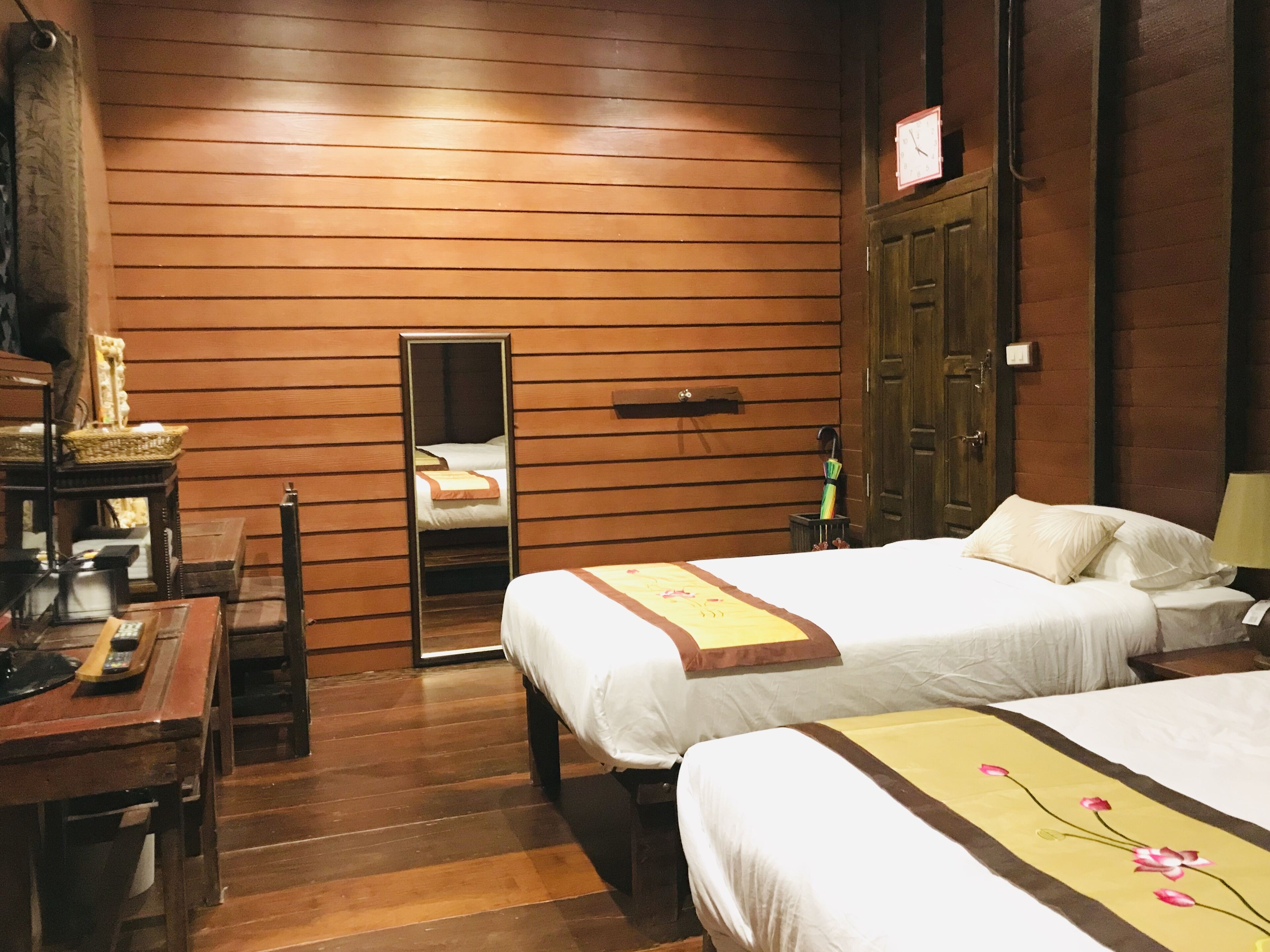 A hotel room with wooden paneling, two beds, a desk, and a mirror.