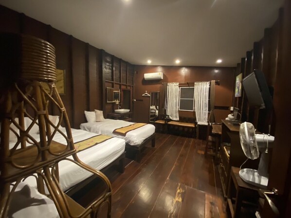 A hotel room with two single beds, a wooden chair, a desk with a computer, and a standing fan. - Reuan Vilawan (Damnoen Saduak)