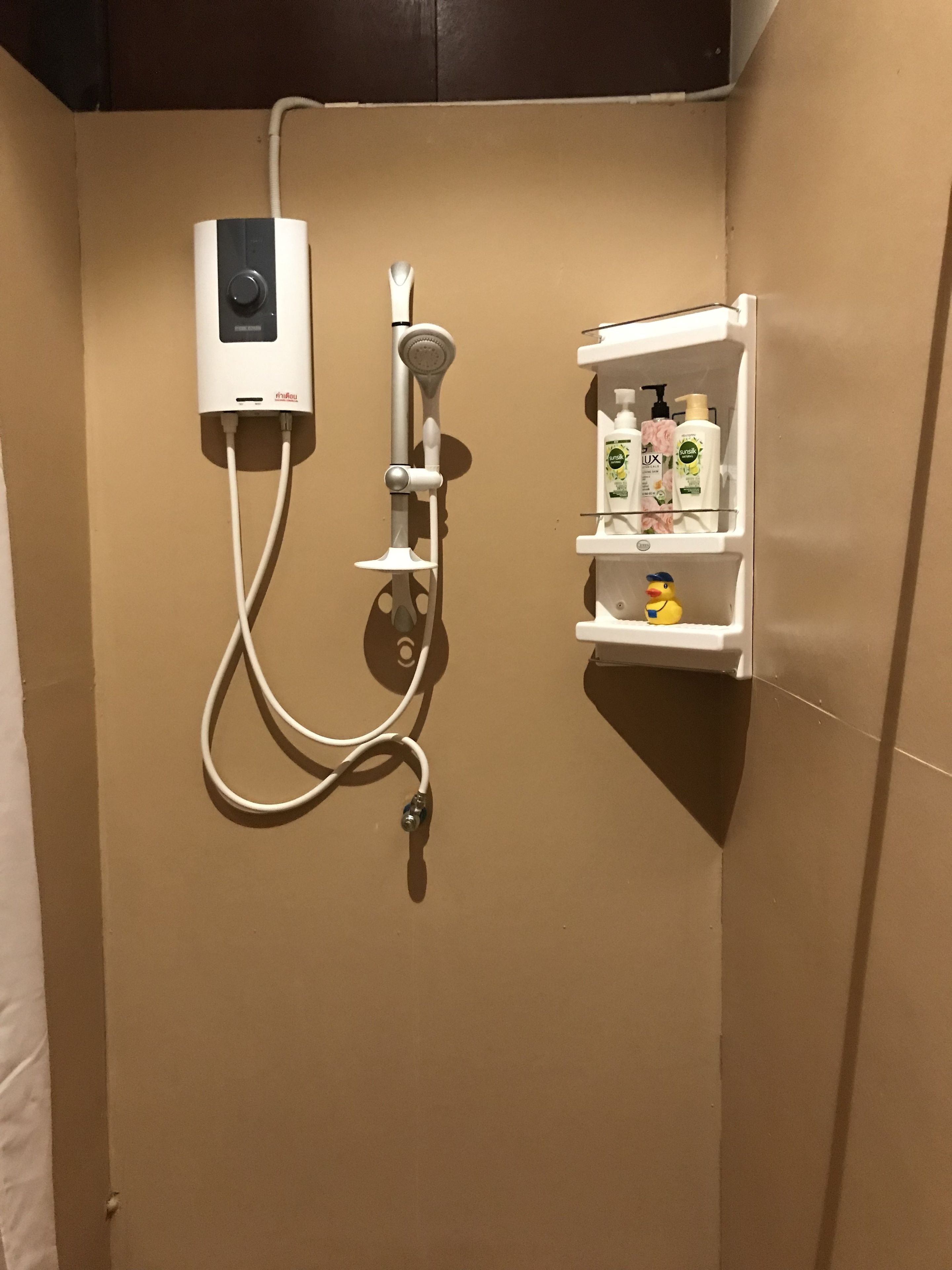 A shower area with a control panel, a handheld showerhead, and a shelf with toiletries.