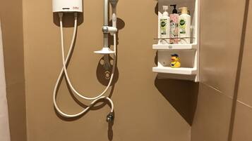 A shower area with a control panel, a handheld showerhead, and a shelf with toiletries.