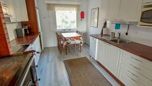 A kitchen with white cabinets, a dining table with chairs, and a window with a view of greenery. - Huitsin nevada by Interhome (Muonio)