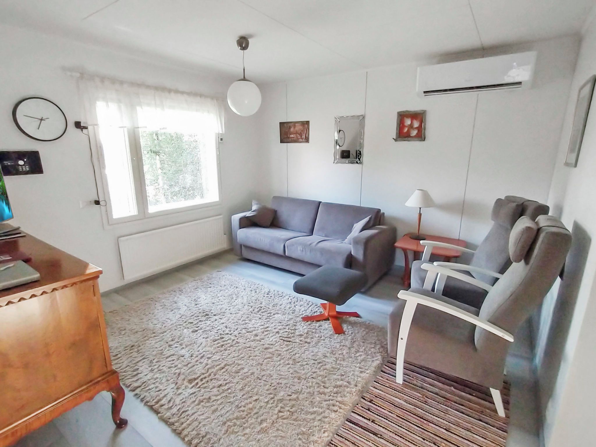 Een woonkamer met een grijze bank, een bijzettafeltje, een lamp en een houten tafeltje.