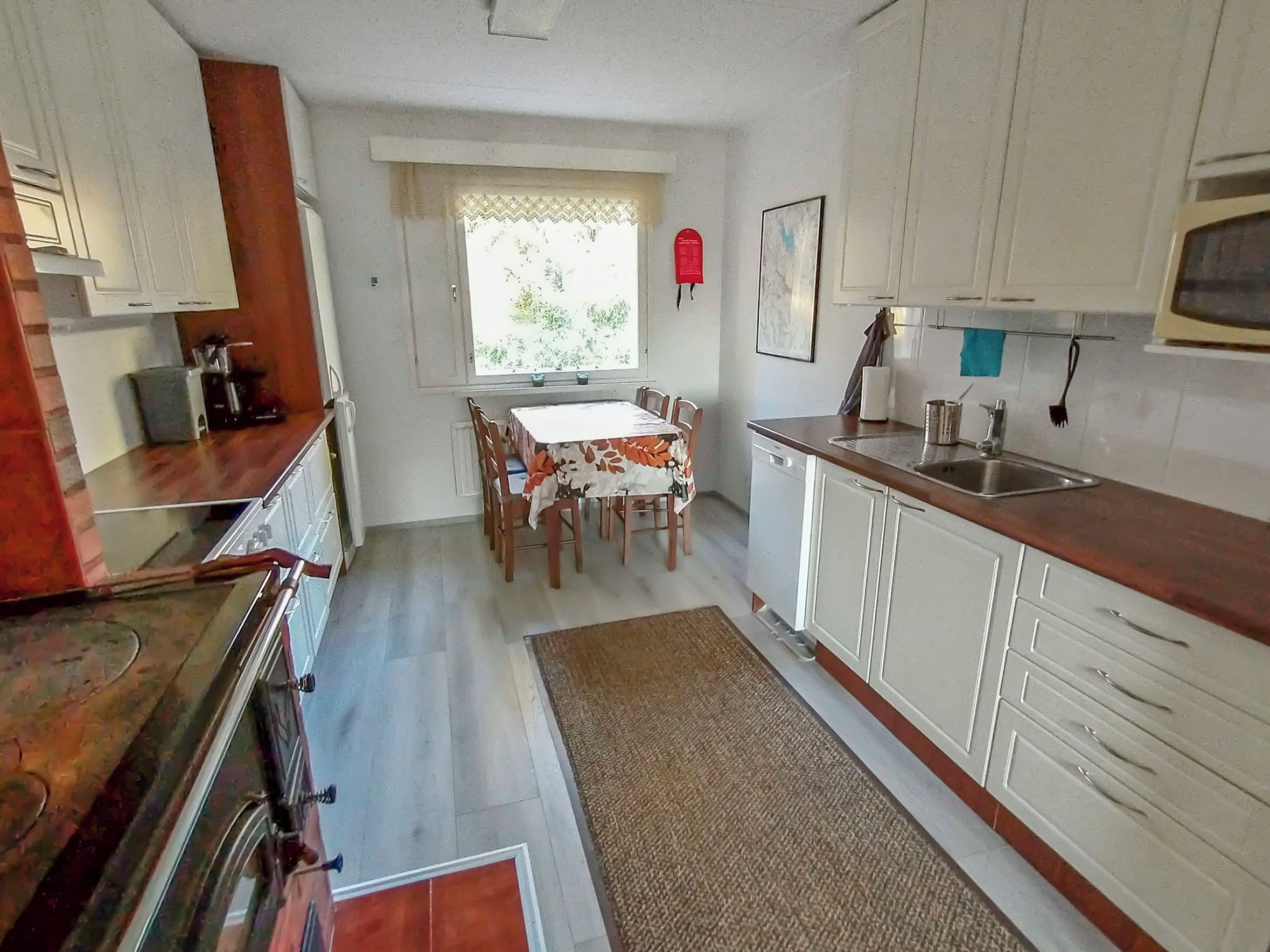 A kitchen with white cabinets, a dining table with chairs, a window with a view, and a red fire extinguisher.