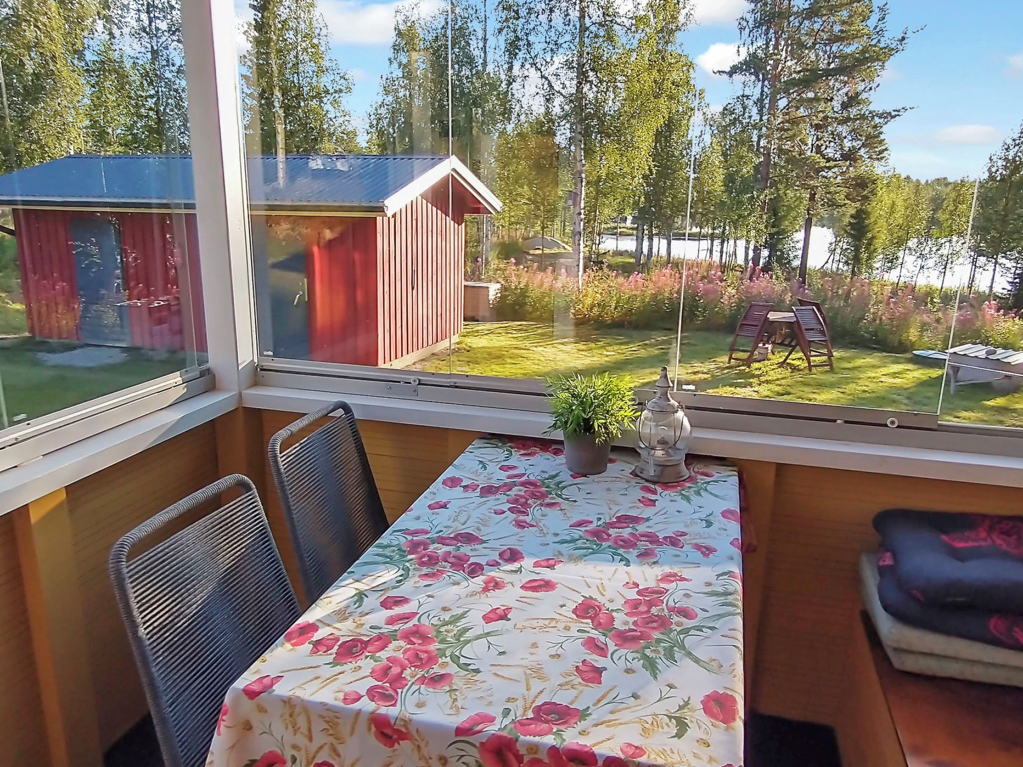 Een kamer met een tafel en stoelen, uitzicht op een tuin en een kleine schuur.