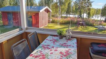Een kamer met een tafel en stoelen, uitzicht op een tuin en een kleine schuur.
