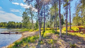 A lakeside cabin with a dock, surrounded by trees and a clear sky.