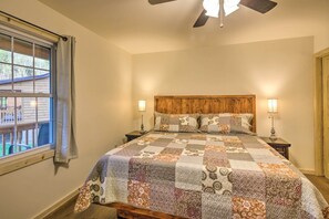 A bedroom with a wooden headboard, a quilted bedspread, two bedside lamps, and a window with curtains. - Private Hot Tub: Tuckasegee River Couple's Escape (Bryson City)