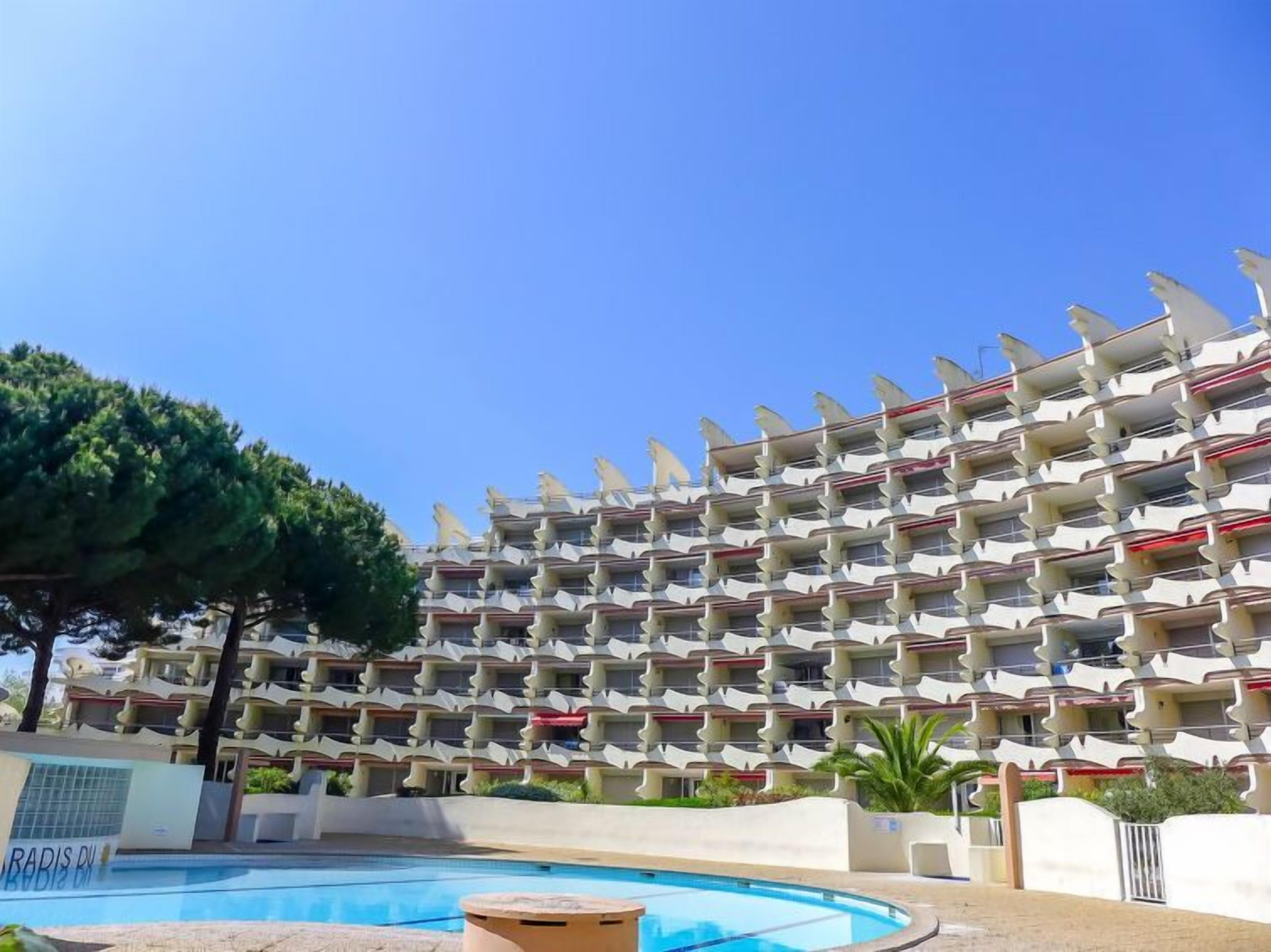 A multi-story hotel with a distinctive wavy facade, a swimming pool, and a clear blue sky.