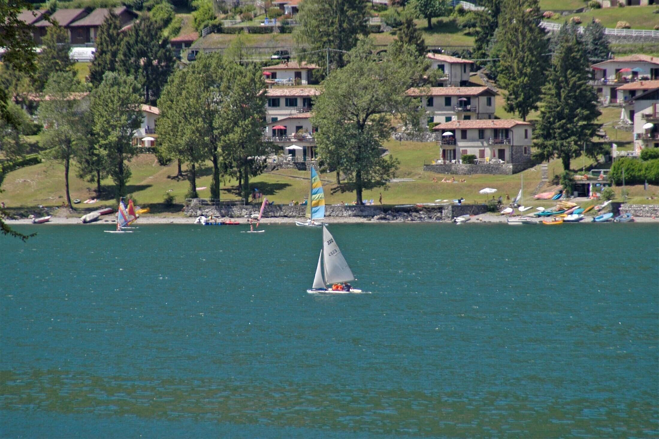 Un voilier sur un lac paisible, avec des maisons et des arbres en arrière-plan.