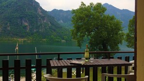 Un tavolo di legno con una bottiglia e dei bicchieri su un balcone che si affaccia su un lago e delle montagne.