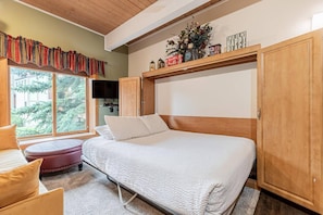 Een slaapkamer met een bed, een raam, een televisie en een plank met decoratieve spullen.