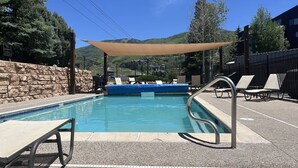 Un área de piscina con sillones de descanso, un muro de piedra y vistas a montañas.