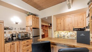 Una cocina moderna con armarios de madera, un refrigerador de acero inoxidable, horno empotrado y una barra con dos taburetes negros.