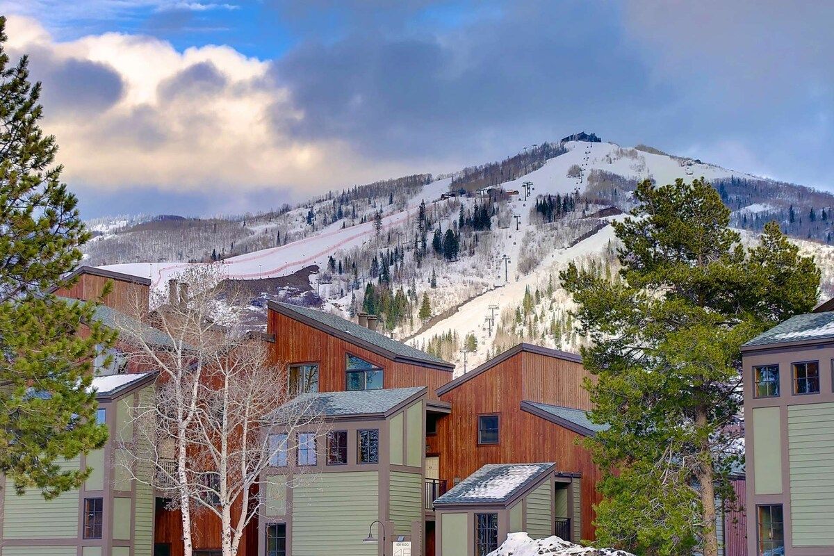 A mountain resort with wooden buildings, a ski slope, and a clear sky.