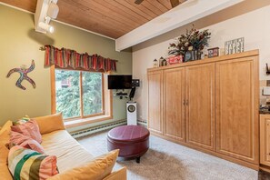 Een gezellige kamer met een bed, een televisie, houten kasten en een raam met uitzicht op bomen.