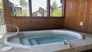 Una bañera de hidromasaje con baranda metálica, tapa de desagüe y pared de madera con ventana.